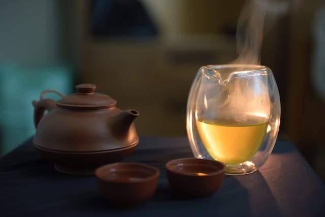 A glass of tea next to a tea pot